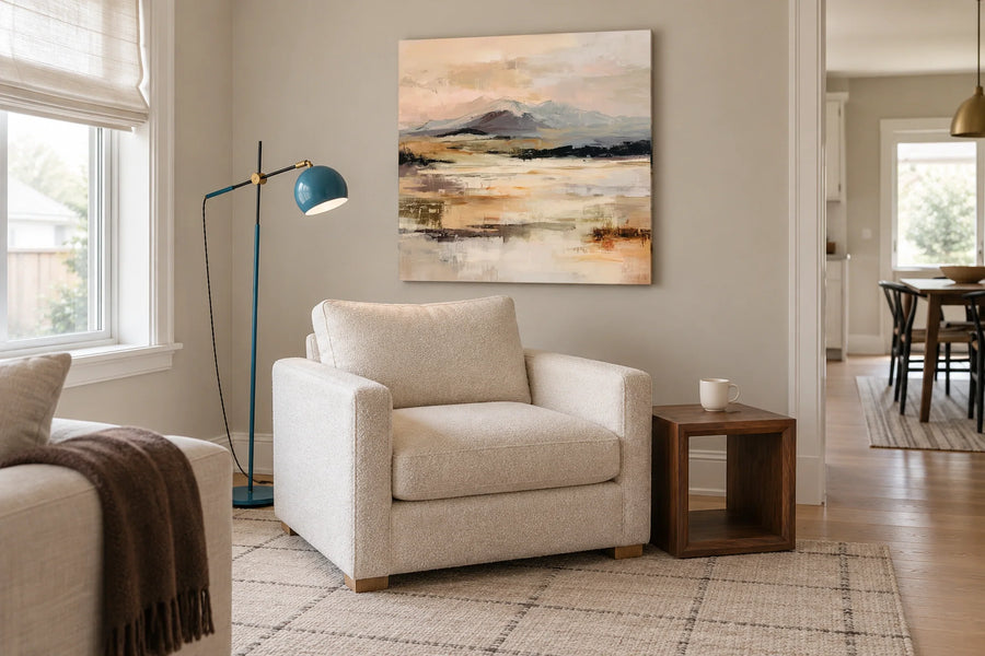 Mountain landscape canvas above a cream reading chair beside a blue floor lamp and walnut side table in a cosy living room.