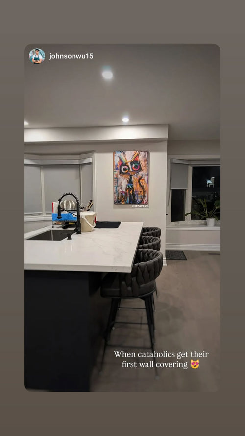 Colourful abstract cat art hanging beside a white kitchen island with dark upholstered stools.