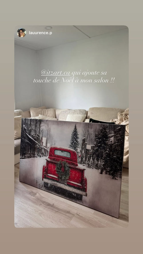 Christmas art print of a red vintage truck with a wreath in a snowy village, leaning against a living room sofa.