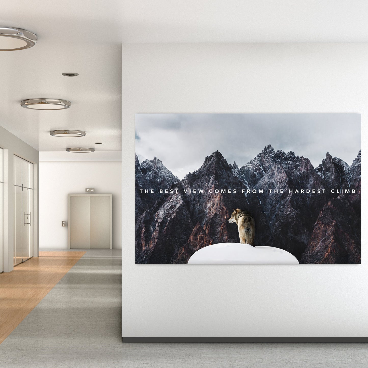 A motivational metal wall art print of a lone wolf on a snowy peak, surrounded by towering rugged mountains, with the text "The best view comes from the hardest climb."
