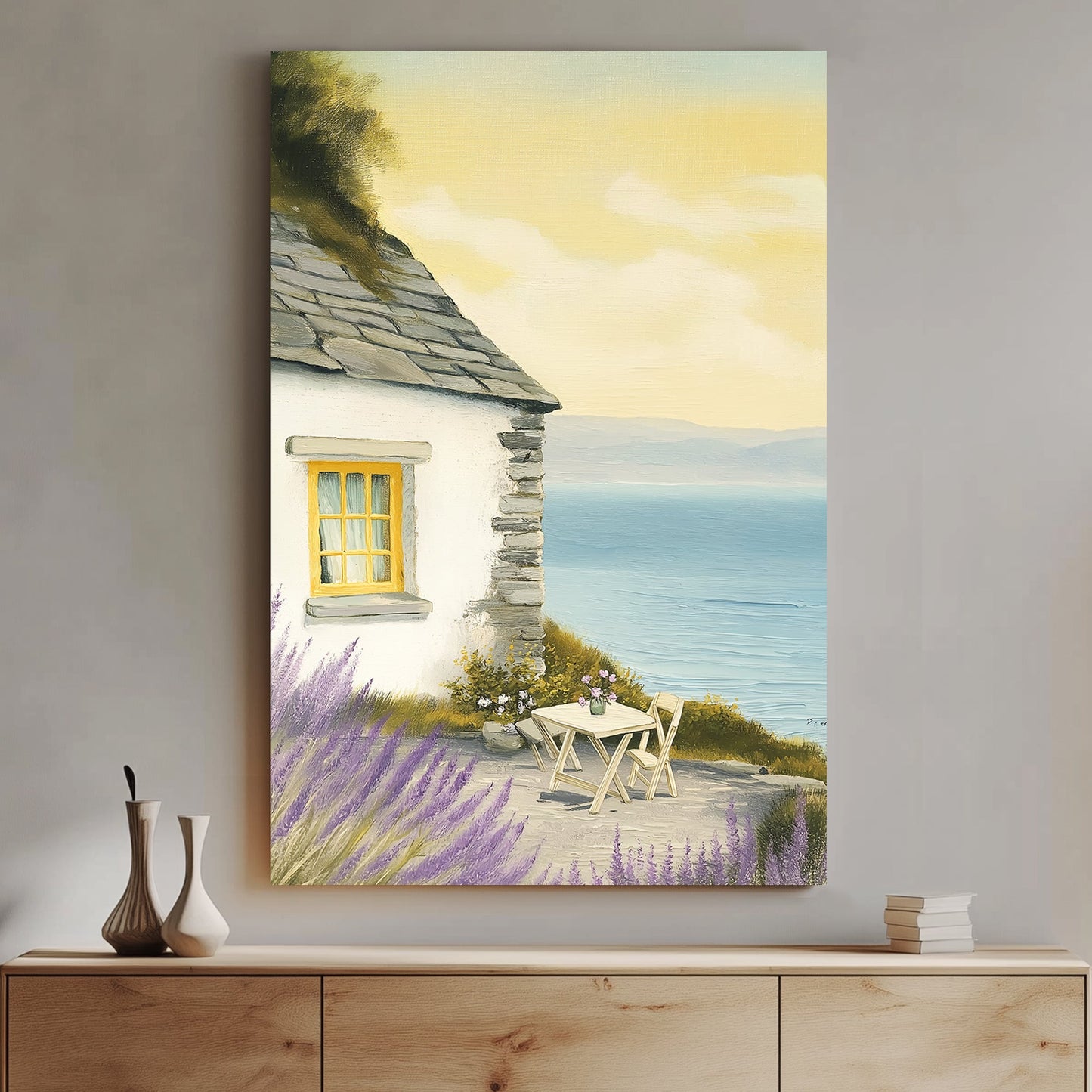 Oil-style wall art of a seaside cottage with a stone wall, lavender bushes, a table set for two, and a view of the ocean under a golden sky.