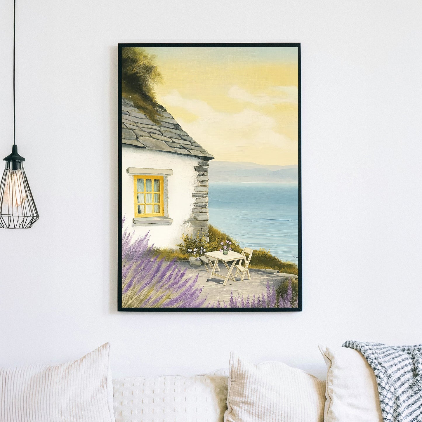 Oil-style wall art of a seaside cottage with a stone wall, lavender bushes, a table set for two, and a view of the ocean under a golden sky.