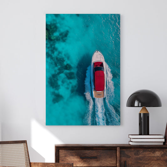Aerial view of a white yacht with a red canopy cruising through turquoise ocean waters, leaving a foamy wake.