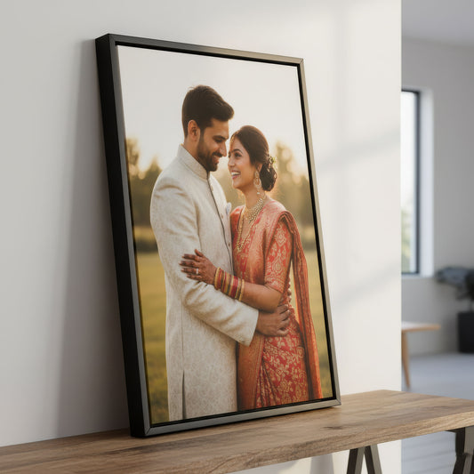 Black framed canvas photo of a couple in traditional attire on a wooden table.