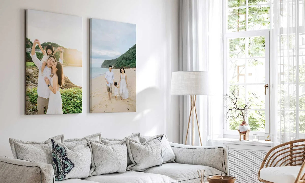 Two vertical framed wall art prints showing beach and outdoor family photographs, displayed above a light gray sofa in a bright modern living room.