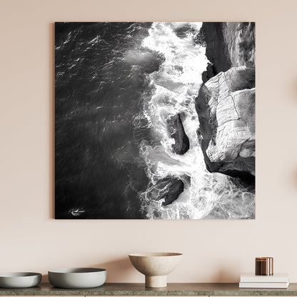 Black and white image of waves crashing against rocky cliffs, creating a dramatic coastal scene.