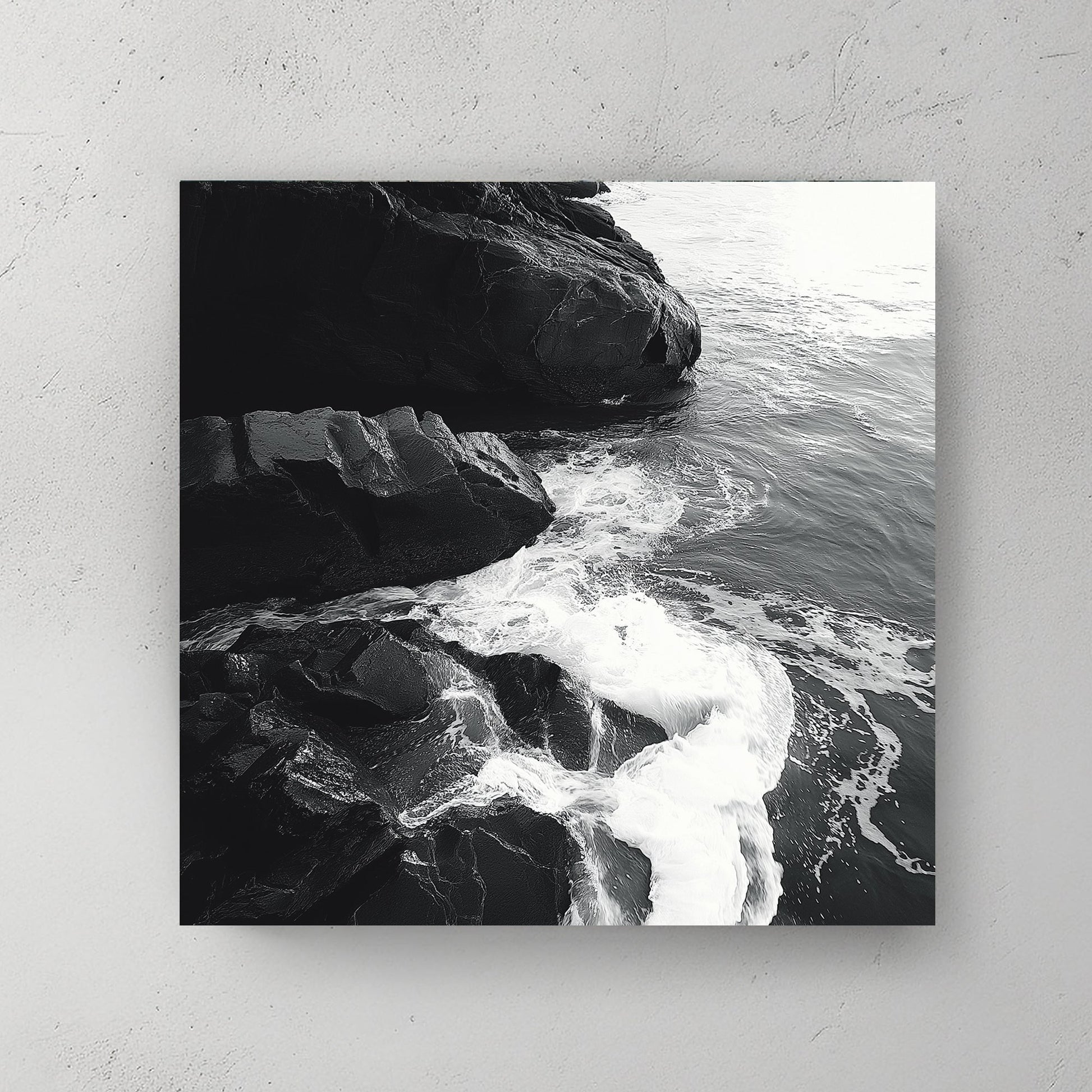 Black and white image of ocean waves splashing against rugged rocks along the shoreline.