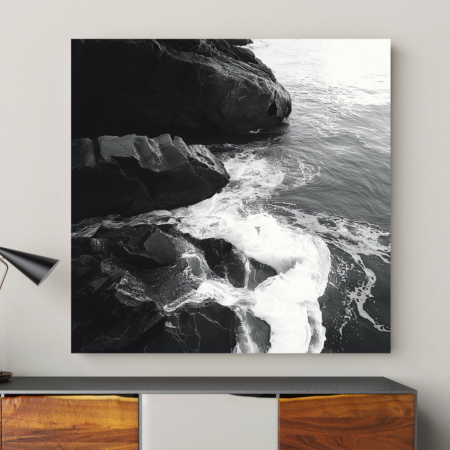 Black and white image of ocean waves splashing against rugged rocks along the shoreline.