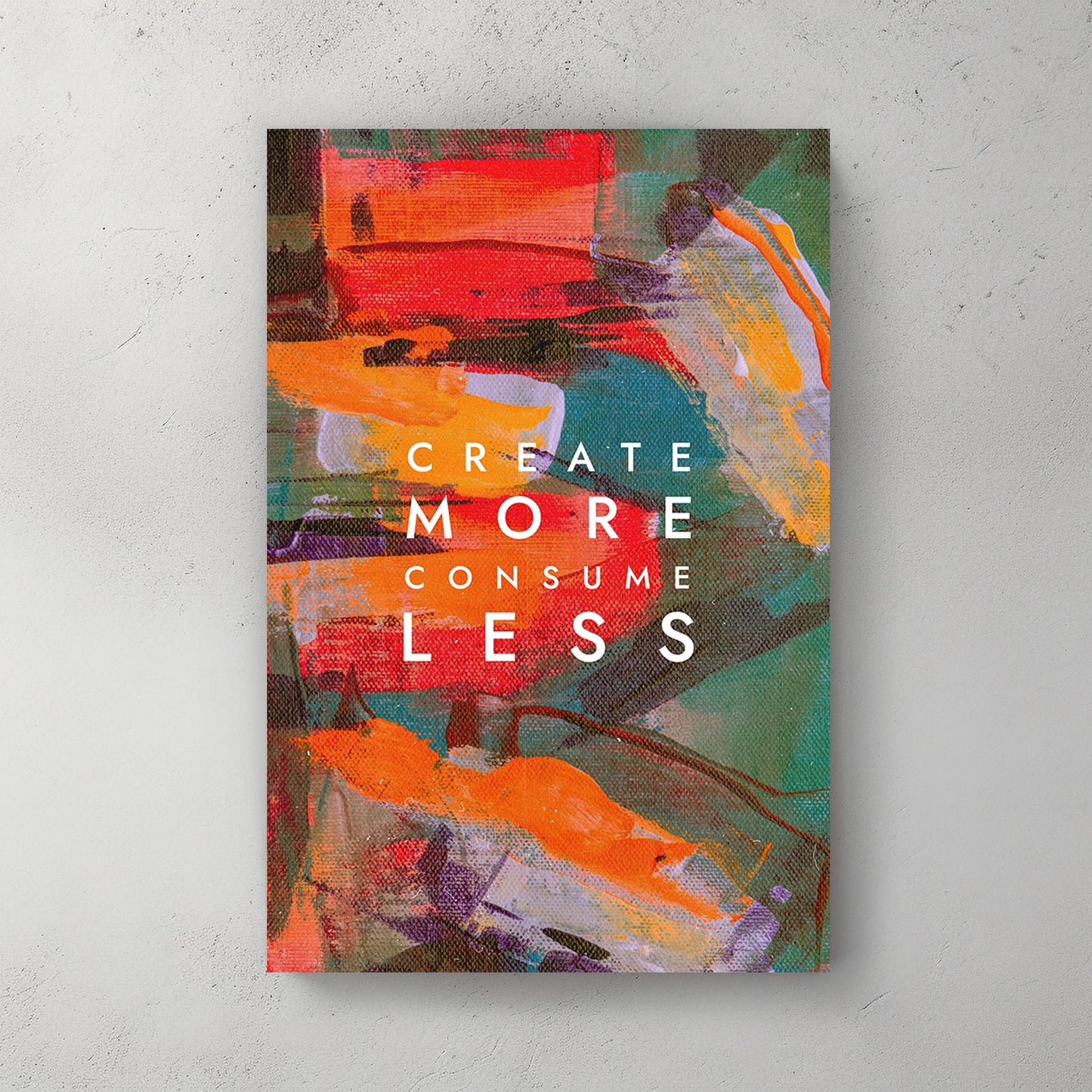 A colourful abstract canvas wall art print with bold strokes of orange, red, and green, overlaid with the motivational text "Create More Consume Less."