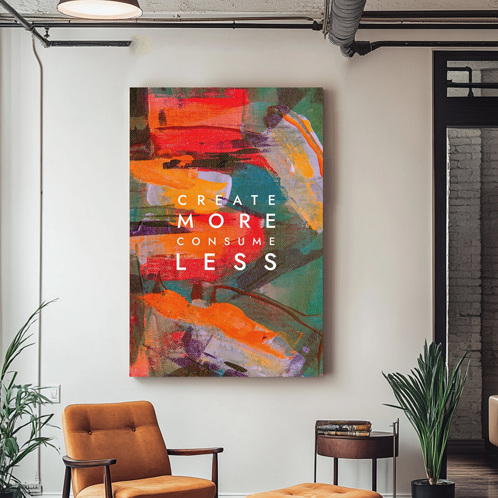 A colourful abstract canvas wall art print with bold strokes of orange, red, and green, overlaid with the motivational text "Create More Consume Less."