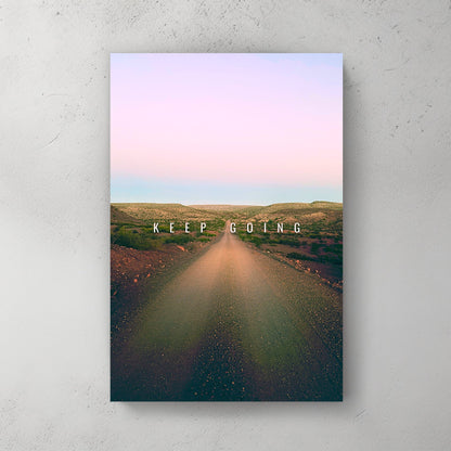 A metal wall art print of a peaceful dirt road stretches into the horizon under a gradient pastel sky, featuring the motivational text "Keep Going."