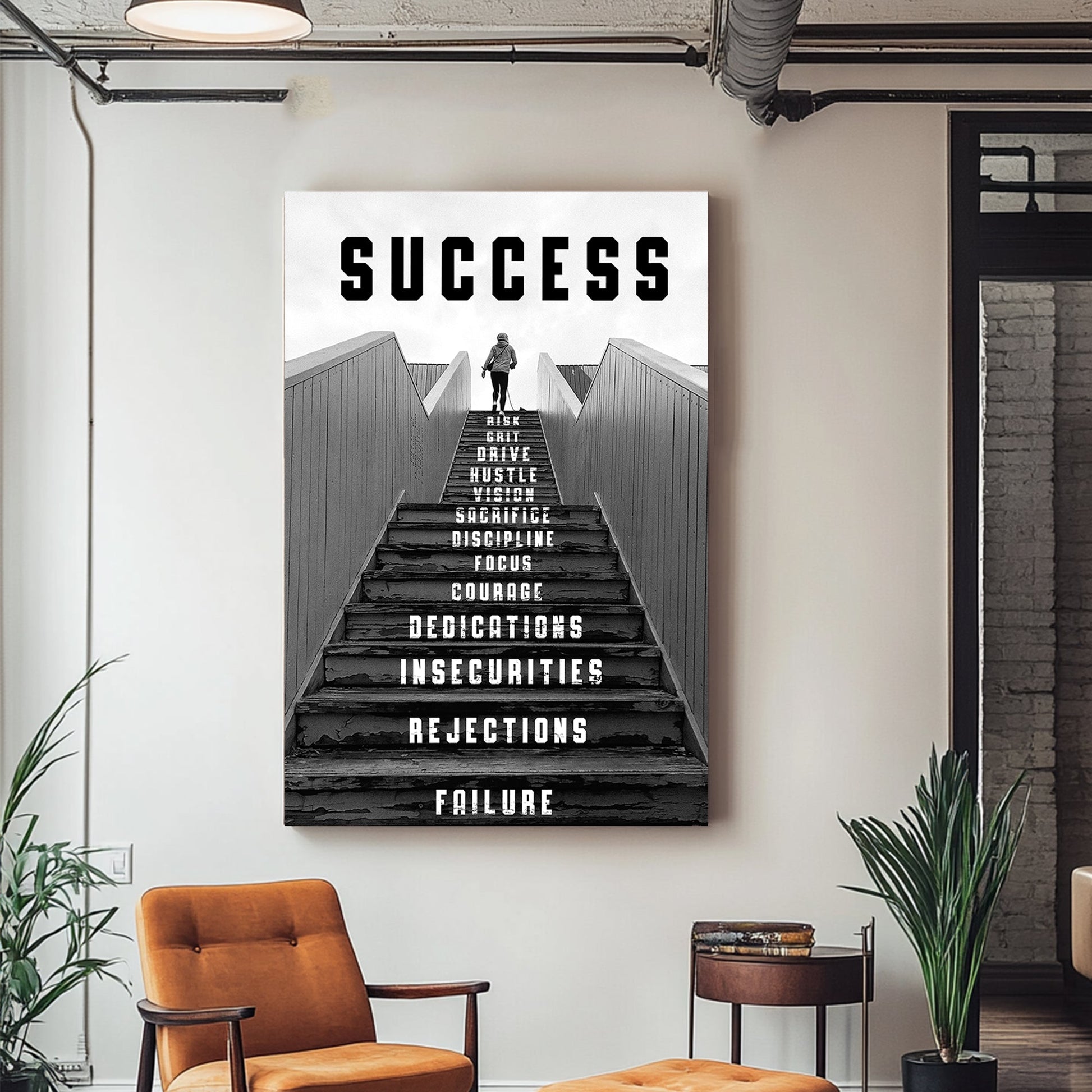 Black-and-white metal wall art print of a person climbing a staircase with motivational words like "risk," "focus," and "dedication" inscribed on the steps, representing the journey to success.