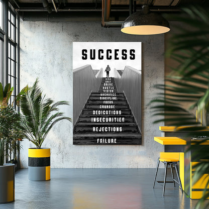 Black-and-white metal wall art print of a person climbing a staircase with motivational words like "risk," "focus," and "dedication" inscribed on the steps, representing the journey to success.