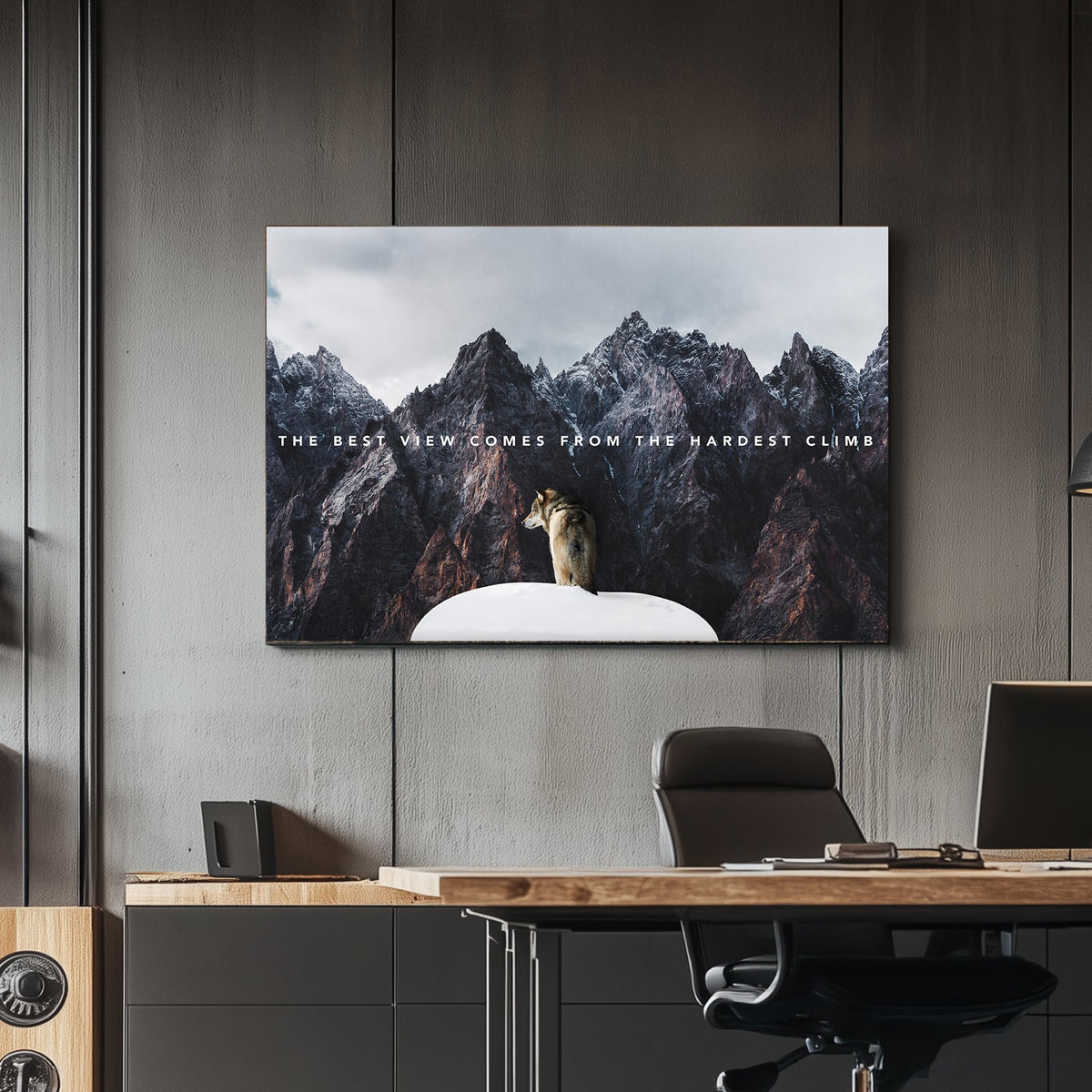 A motivational metal wall art print of a lone wolf on a snowy peak, surrounded by towering rugged mountains, with the text "The best view comes from the hardest climb."
