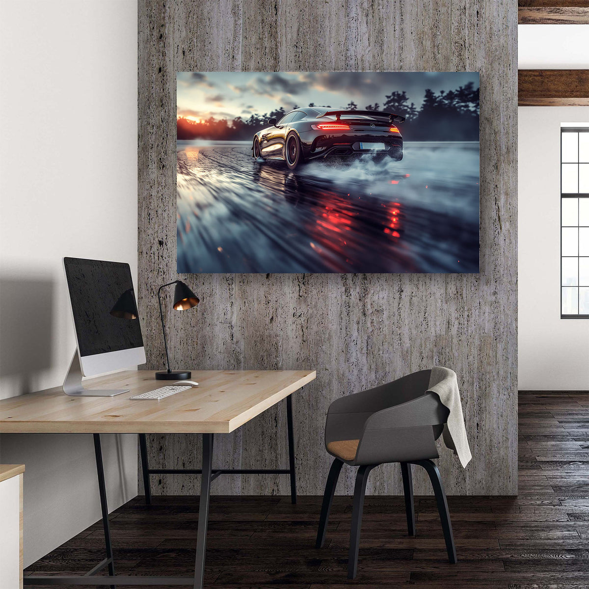 A large rectangular wall art print showing a dark sports car drifting on a wet reflective road at sunset, displayed on a textured gray wall above a wooden desk in a modern office interior.