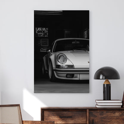 A black-and-white digital wall art print of a silver Porsche emerging from the shadows of a dimly lit garage, showcasing its refined curves and elegance.