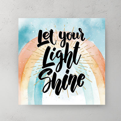 A motivational typography wall art print with the phrase “Let Your Light Shine” in bold script, set against a pastel watercolour rainbow with golden rays.