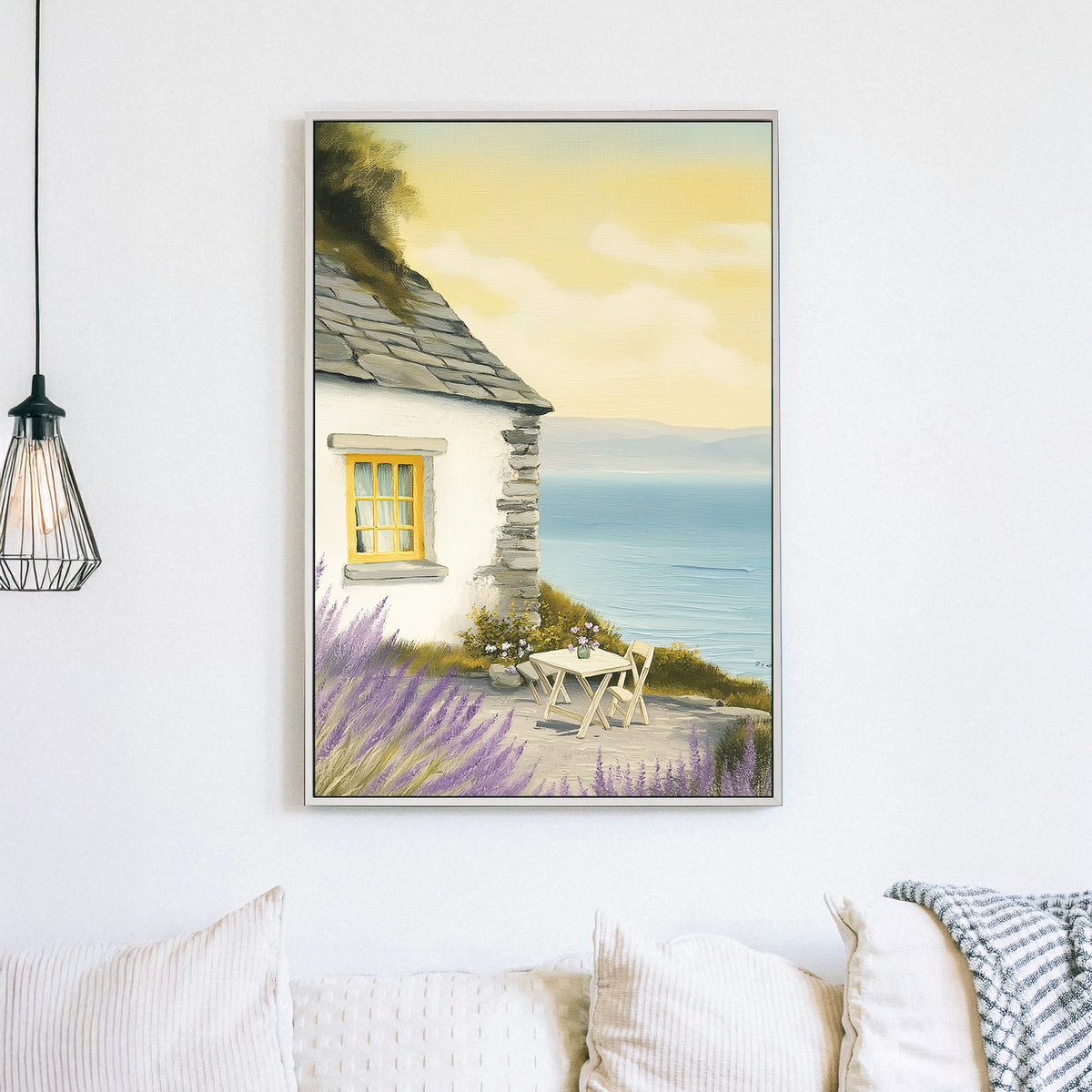 Oil-style wall art of a seaside cottage with a stone wall, lavender bushes, a table set for two, and a view of the ocean under a golden sky.