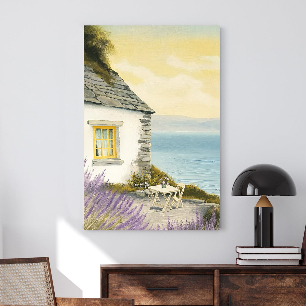 Oil-style wall art of a seaside cottage with a stone wall, lavender bushes, a table set for two, and a view of the ocean under a golden sky.