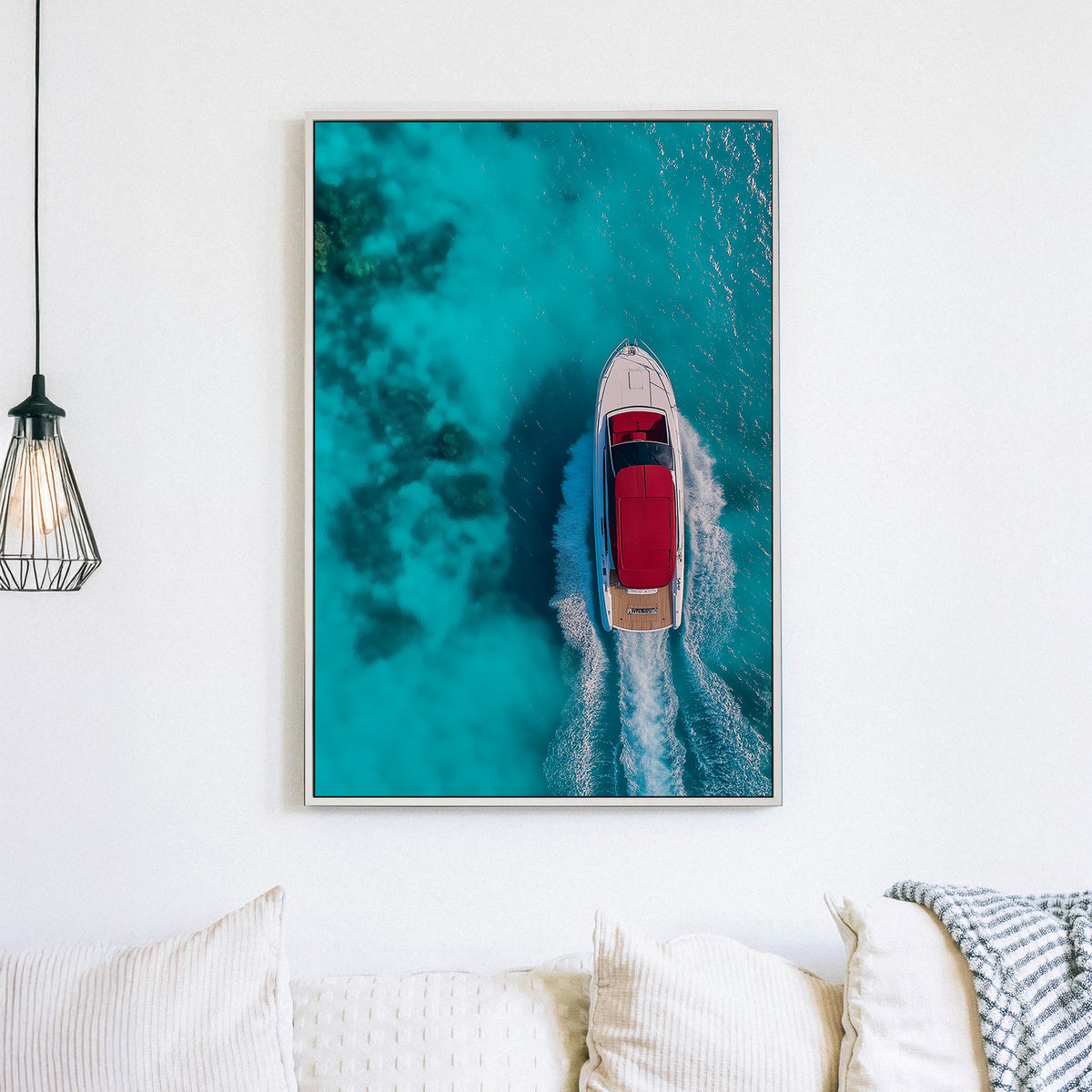 Aerial view of a white yacht with a red canopy cruising through turquoise ocean waters, leaving a foamy wake.