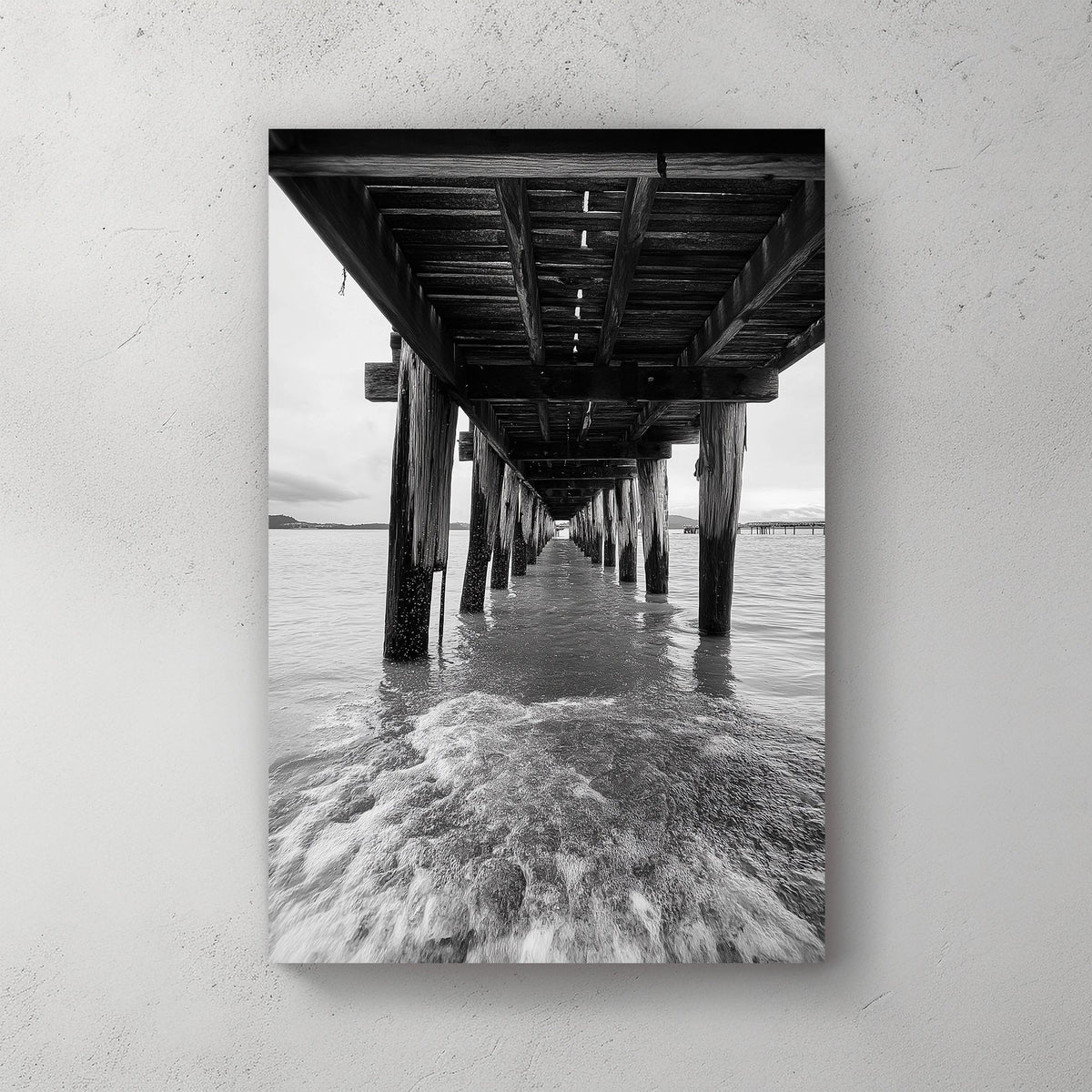 black and white wall art photography of ocean waves under wooden pier with vanishing point perspective