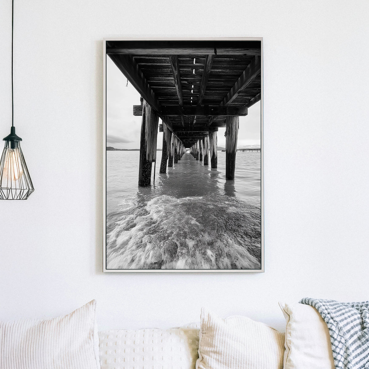 black and white wall art photography of ocean waves under wooden pier with vanishing point perspective