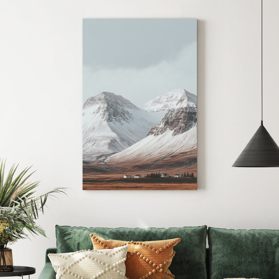 Snowy mountain landscape with cabins on a golden plain beneath grey skies