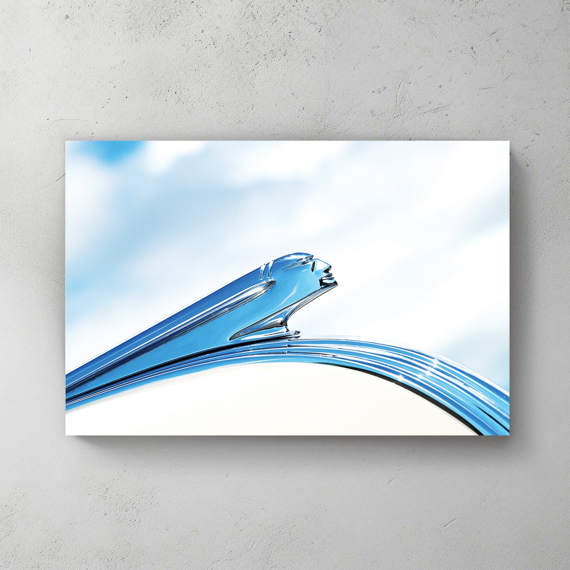 Art Deco chrome Pontiac hood ornament, a streamlined winged figure in polished silver against soft blue sky and cloud — canvas wall art print