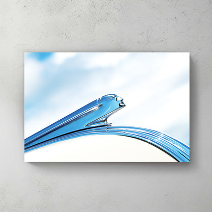 Art Deco chrome Pontiac hood ornament, a streamlined winged figure in polished silver against soft blue sky and cloud — canvas wall art print
