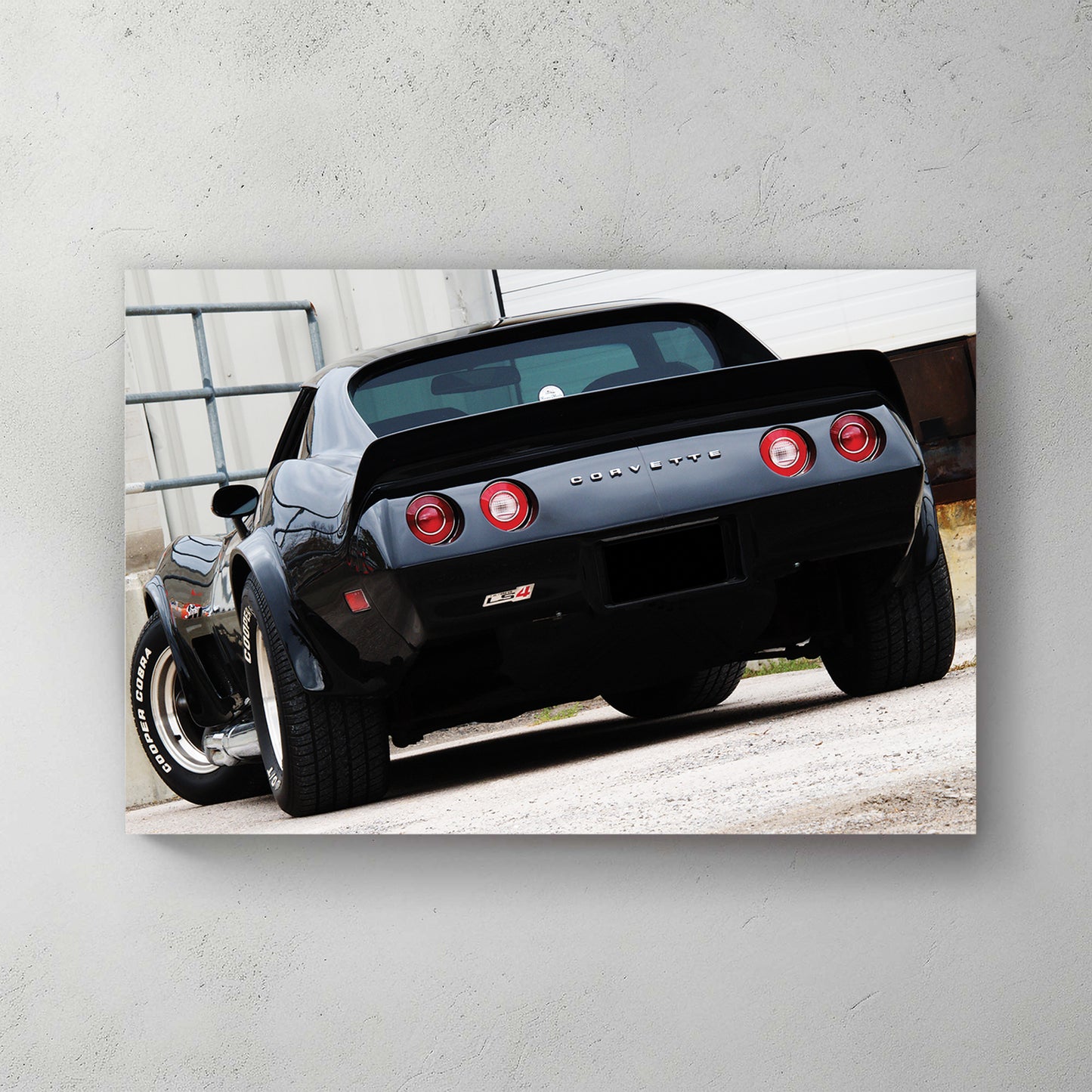 Glossy black C3 Corvette rear, round red taillights and chrome CORVETTE script, parked on gravel — canvas wall art print