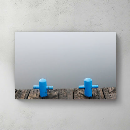 Two blue cross-shaped dock cleats on a weathered wooden dock, calm grey water dissolving into fog — canvas wall art print