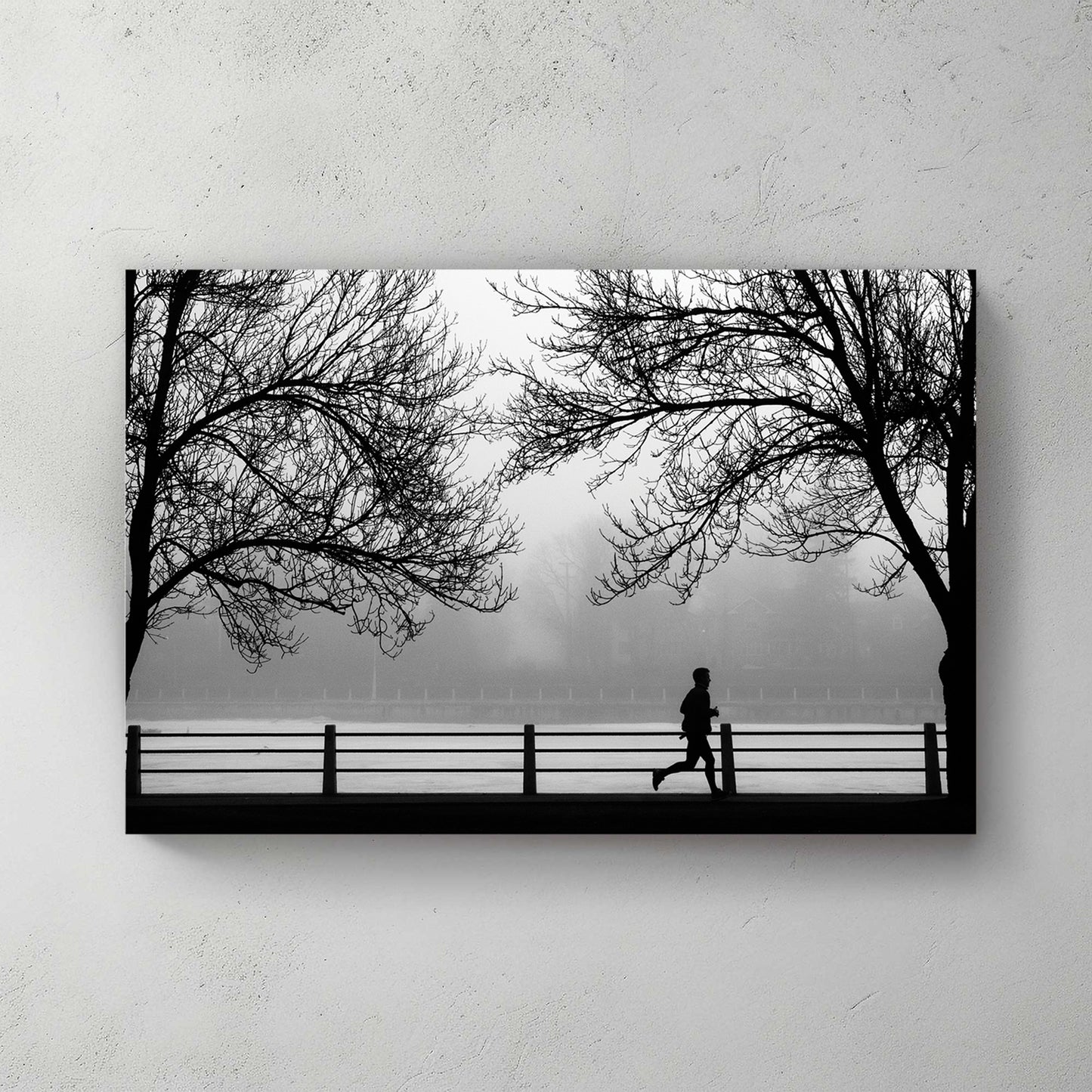 Silhouette of a lone jogger between two bare trees along a misty riverfront railing, moody grey — canvas wall art print