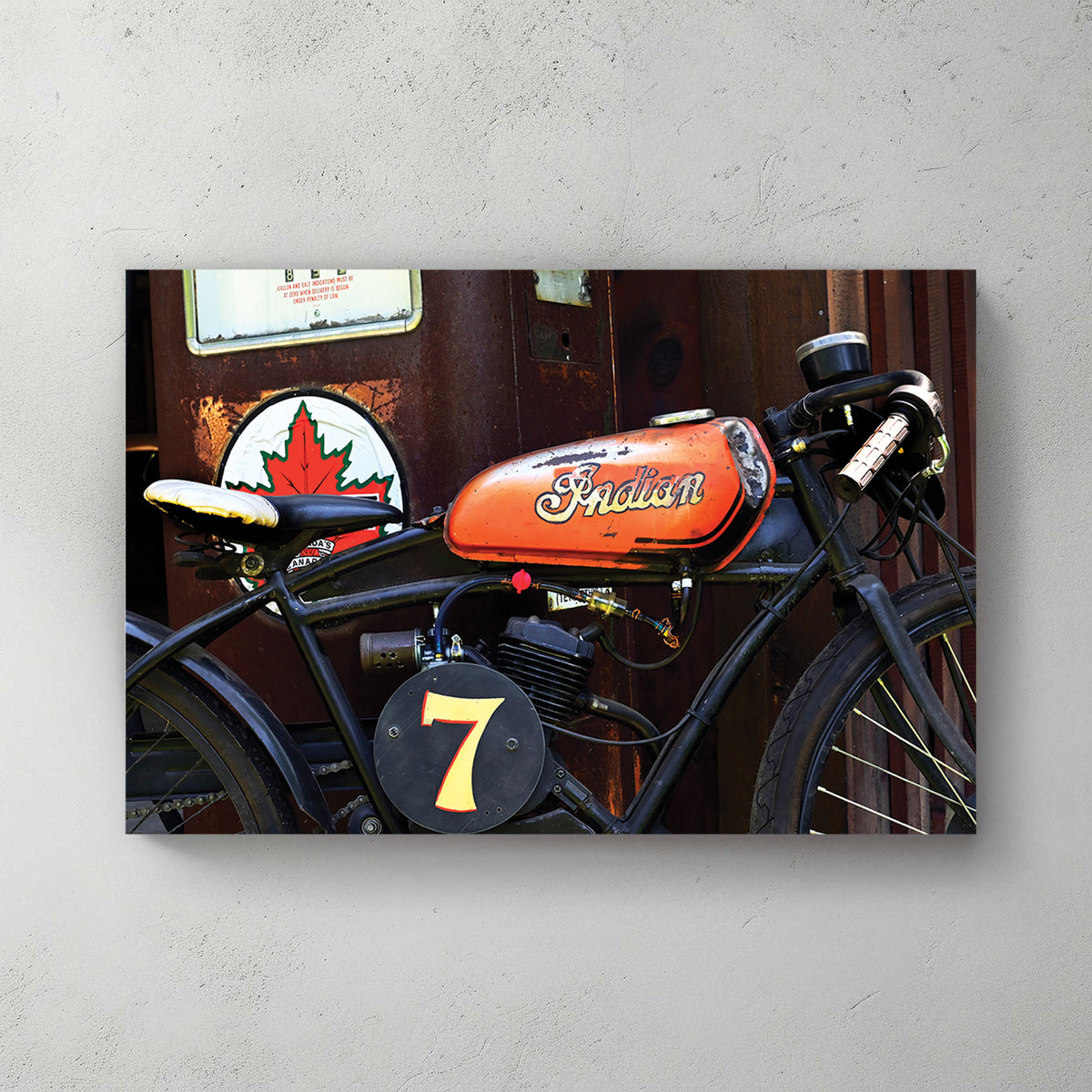Weathered orange-tank Indian racer, number 7 plate, parked by an old Canadian gas pump and maple-leaf sign — canvas wall art print