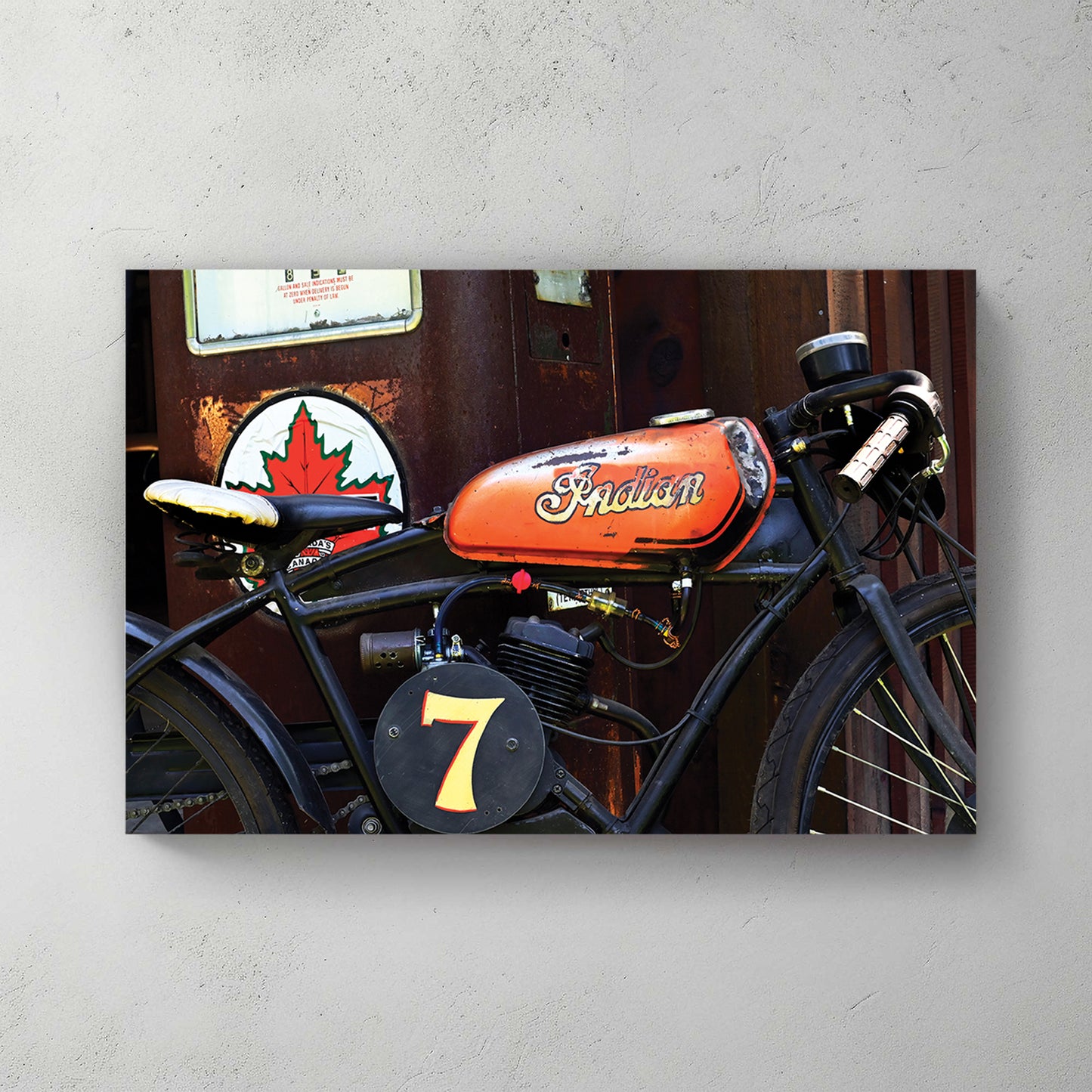Weathered orange-tank Indian racer, number 7 plate, parked by an old Canadian gas pump and maple-leaf sign — canvas wall art print