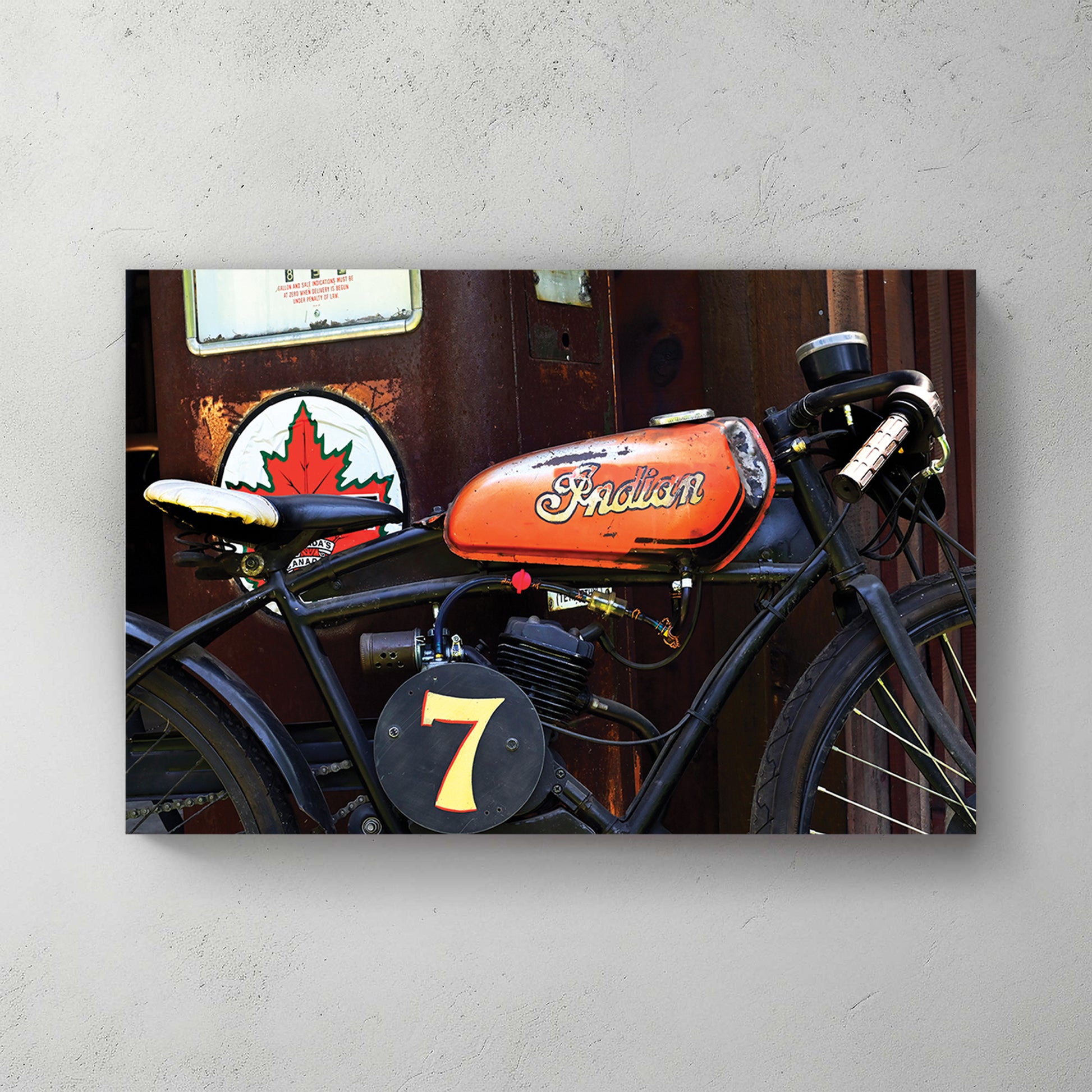 Weathered orange-tank Indian racer, number 7 plate, parked by an old Canadian gas pump and maple-leaf sign — canvas wall art print