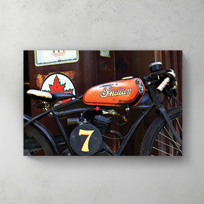 Weathered orange-tank Indian racer, number 7 plate, parked by an old Canadian gas pump and maple-leaf sign — canvas wall art print