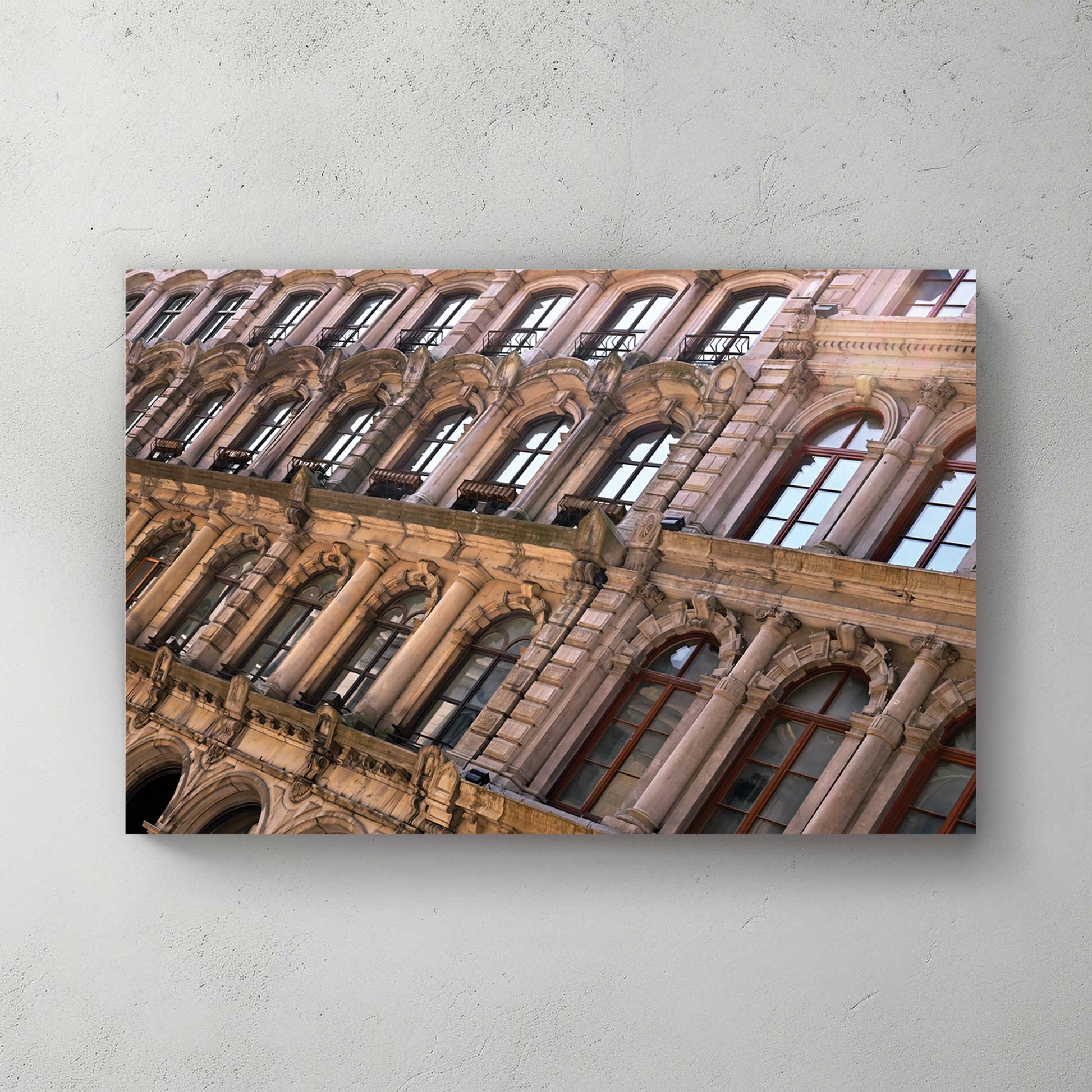 Angled view up an ornate Beaux-Arts stone building, rows of arched and columned windows in warm light — canvas wall art print