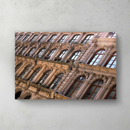 Angled view up an ornate Beaux-Arts stone building, rows of arched and columned windows in warm light — canvas wall art print