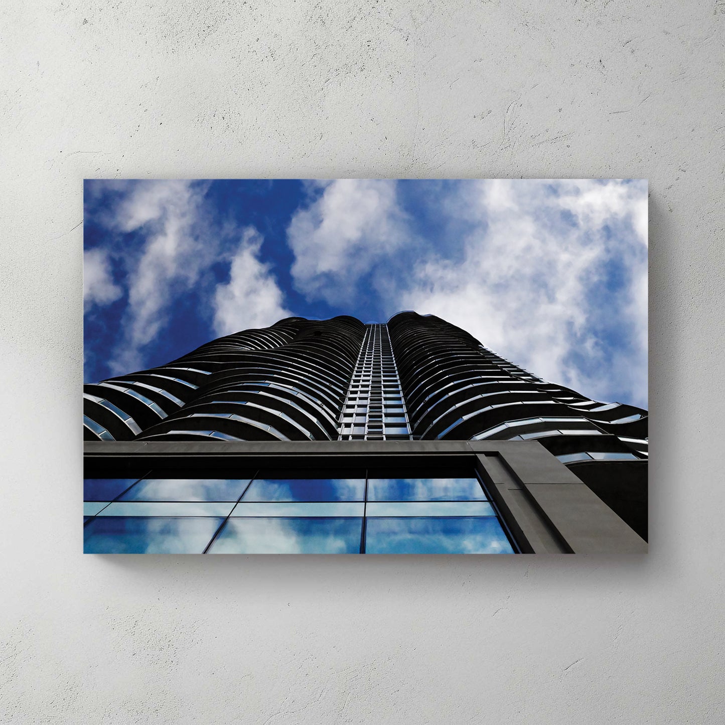Looking straight up a curved black condo tower into a dramatic blue-and-white cloudy sky — canvas wall art print