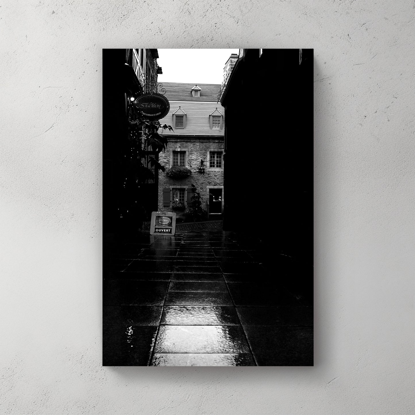 Moody black-and-white wet cobblestone alley in Old Quebec, a lit stone shopfront glowing at the end — canvas wall art print