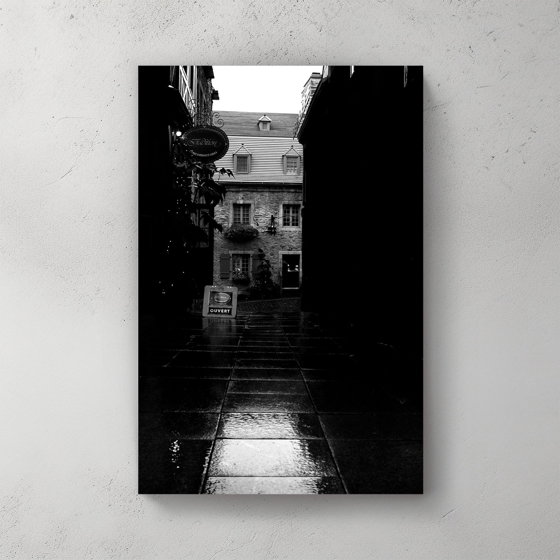 Moody black-and-white wet cobblestone alley in Old Quebec, a lit stone shopfront glowing at the end — canvas wall art print