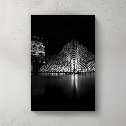 Black-and-white Louvre glass pyramid lit at night, mirrored in the courtyard pool beside the old palace — canvas wall art print