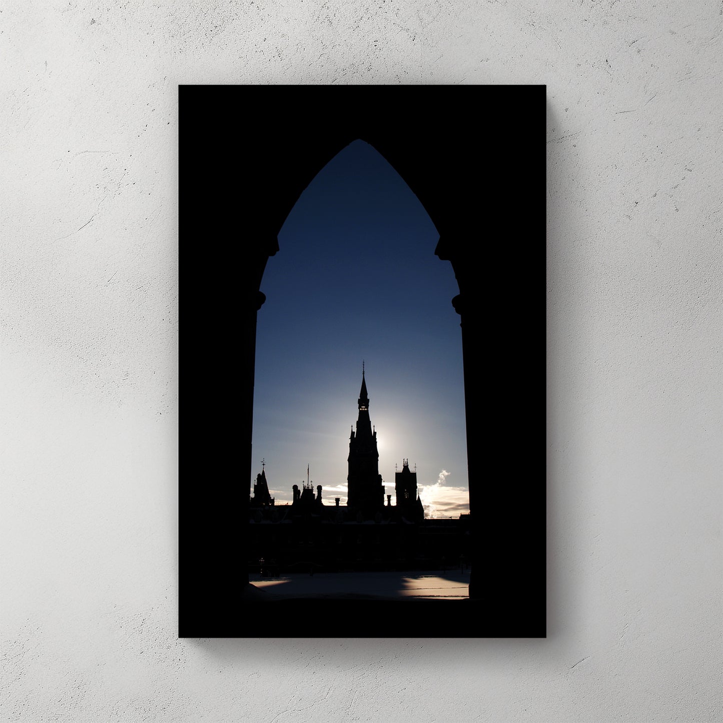 Ottawa's Parliament spire framed in a Gothic stone arch, backlit by a pale winter sun — canvas wall art print