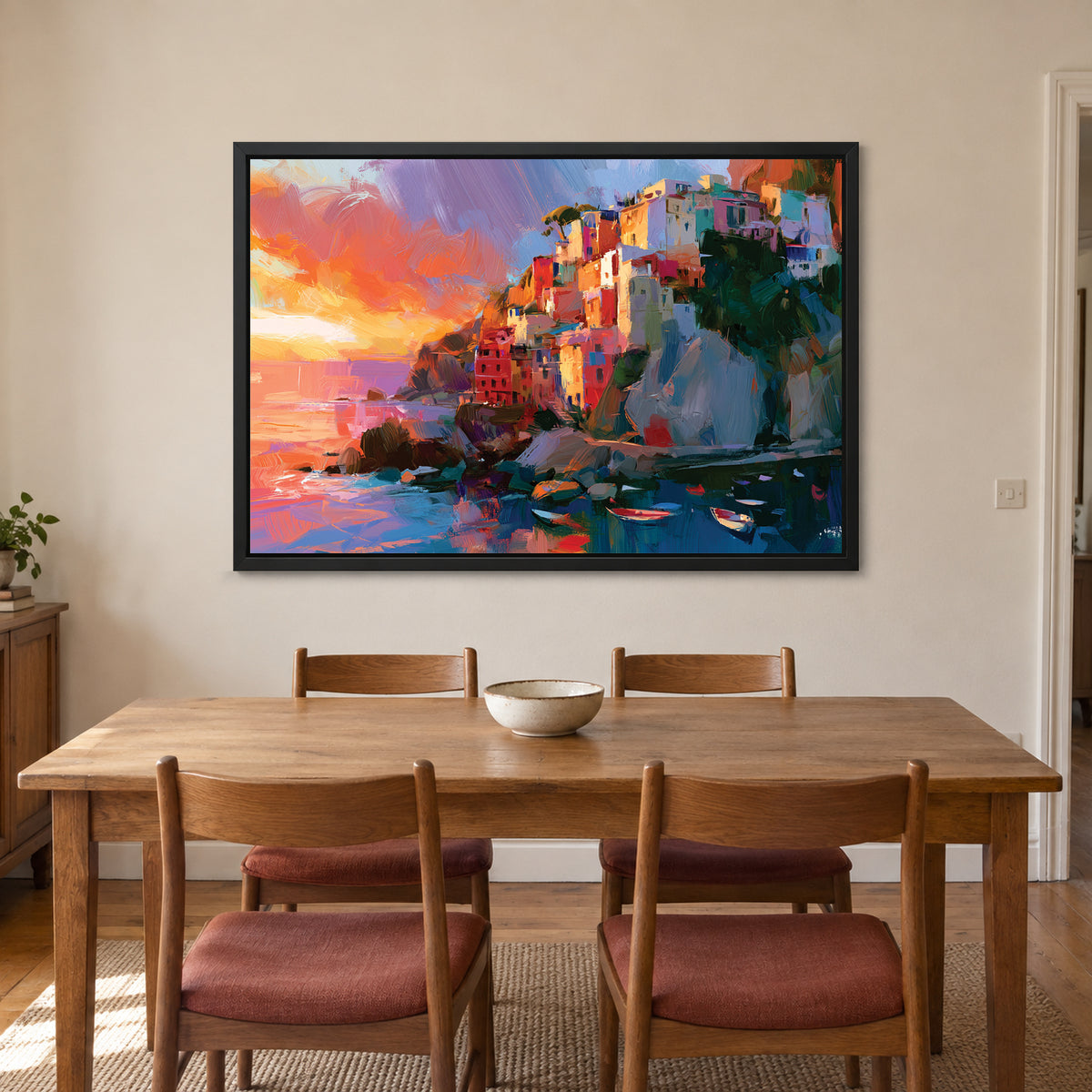 Mediterranean Cliff Harbour Coastal framed canvas in a black floating frame above a wooden dining table with rust-cushioned chairs