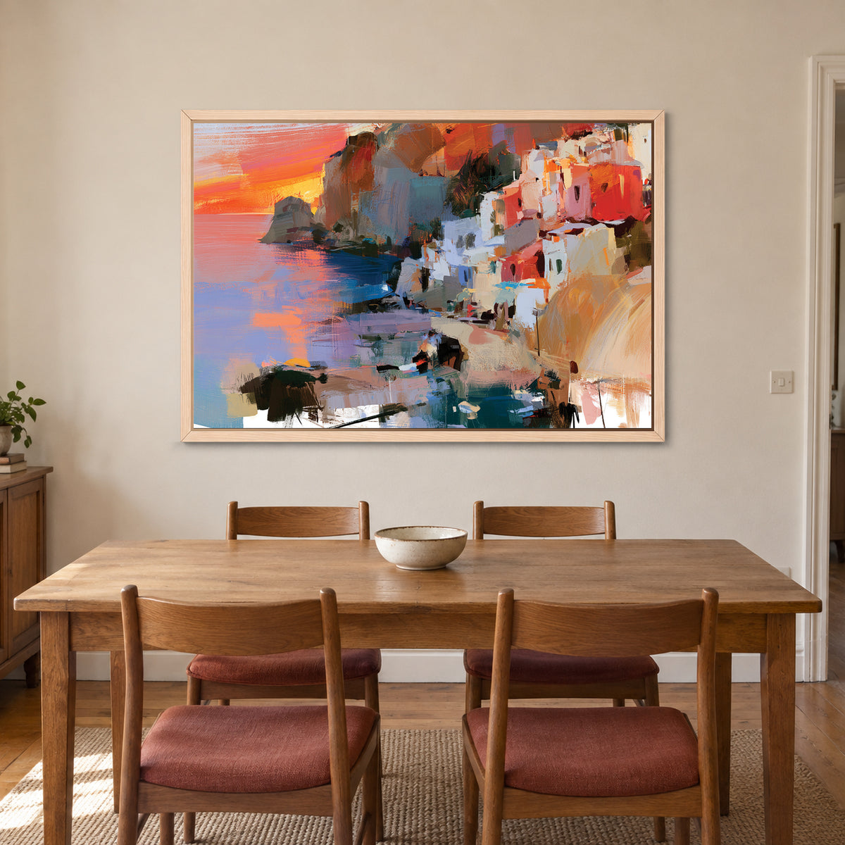 Coastal Town Sunset Headland framed canvas in a natural wood floating frame above a wooden dining table with rust-cushioned chairs