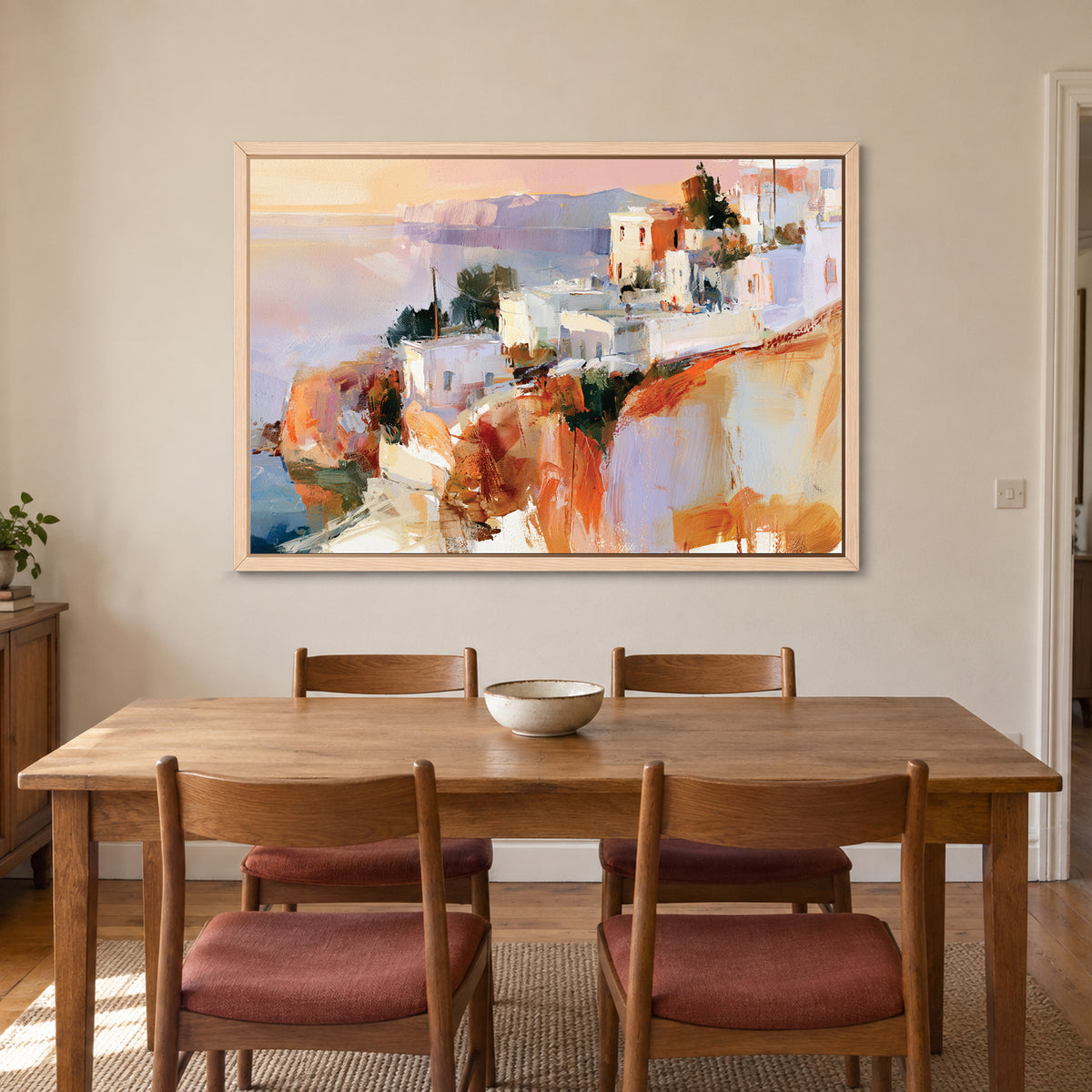 Greek Island Cliff Town framed canvas in a natural wood floating frame above a wooden dining table with rust-cushioned chairs