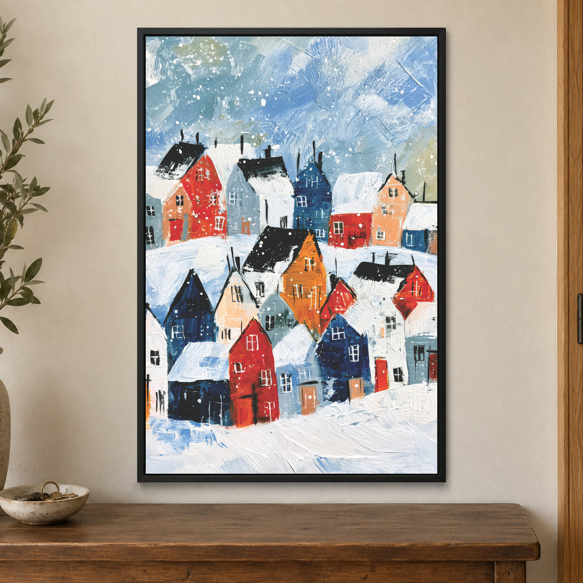 Snowfall Over the Rooftops framed canvas in a black floating frame on a cream wall above a wooden sideboard beside a door frame
