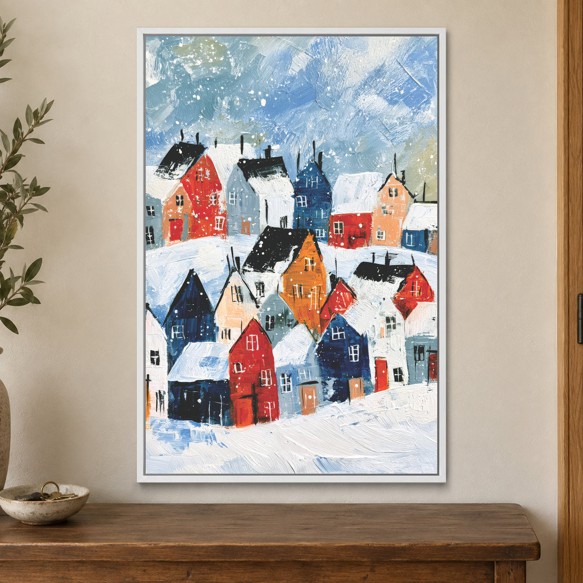 Snowfall Over the Rooftops framed canvas in a white floating frame on a cream wall above a wooden sideboard beside a door frame