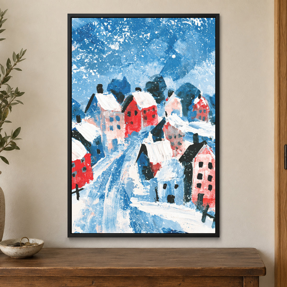 Winter Lane Between the Houses framed canvas in a black floating frame on a cream wall above a wooden sideboard beside a door frame