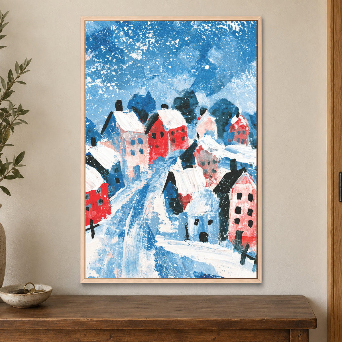 Winter Lane Between the Houses framed canvas in a natural wood floating frame on a cream wall above a wooden sideboard beside a door frame